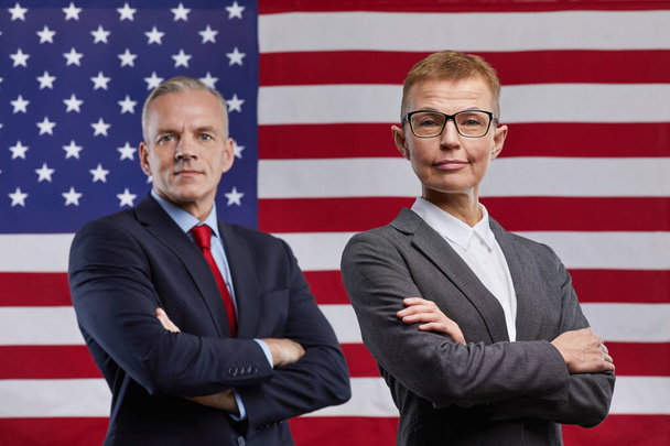 Портрет зрілого чоловіка і жінок політиків, що дивляться на камеру, стоячи зі схрещеними на тлі прапора США, копіюйте простір. - Фото, зображення