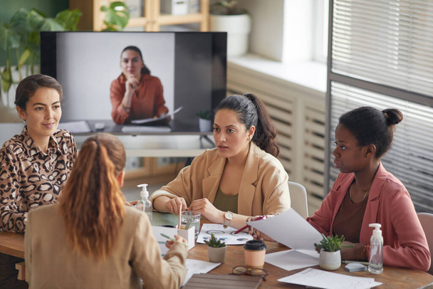 High angle view op multi-etnische groep van zakenvrouwen bespreken project tijdens een vergadering in functie met externe deelnemer in de achtergrond, kopiëren ruimte - Foto, afbeelding