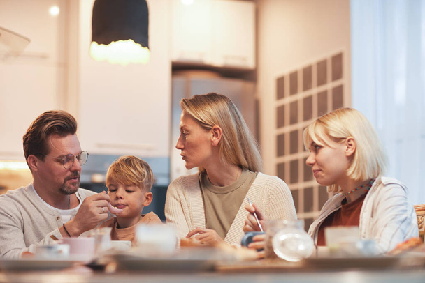 Portrét moderní šťastné rodiny se snídaní společně sedí u stolu v útulném kuchyňském interiéru, rodiče se dvěma dětmi, kopírovací prostor - Fotografie, Obrázek