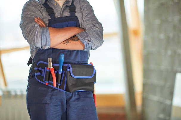 Cropped portrait of contemporary female worker standing with arms crossed with focus on tool belt, copy space - Photo, Image