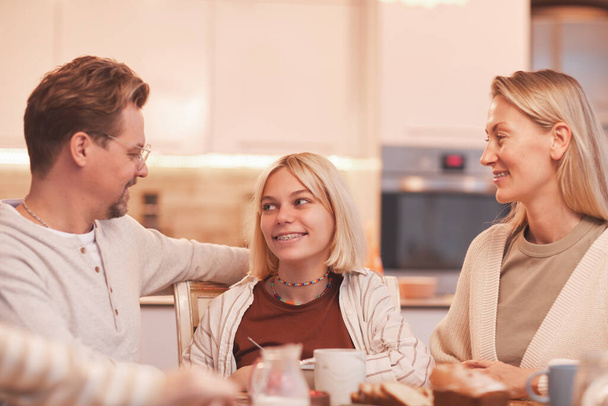 Portrait of mother and father looking at smiling teenage girl while enjoying breakfast together in cozy kitchen interior - Foto, Bild