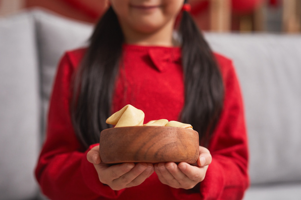 Środek sekcja zbliżenie strzał nierozpoznawalny Azjata dziewczyna w czerwieni z dwoma kucykami trzyma drewniany miska pełna ciasteczka wróżba - Zdjęcie, obraz