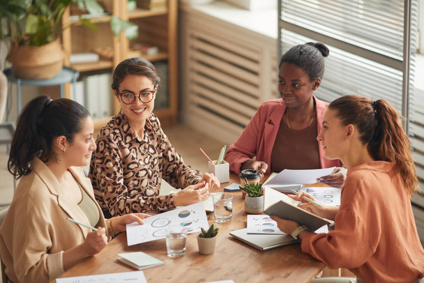 Высокоугловой портрет успешной женской бизнес-команды, обсуждающей работу за столом заседаний и радостно улыбающейся, копирующей пространство - Фото, изображение