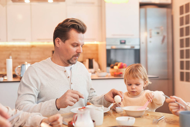 Portret nowoczesnej rodziny korzystających śniadanie razem w kuchni, skupić się na ojcu pomaga cute baby girl, przestrzeń do kopiowania - Zdjęcie, obraz