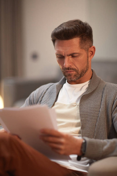 Retrato vertical de hombre de negocios maduro guapo mirando documentos mientras trabaja desde casa - Foto, imagen
