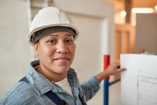 Közelkép egy vegyes bőrű női munkásról, aki keménykalapot visel az építkezésen, fénymásolja a helyet. - Fotó, kép