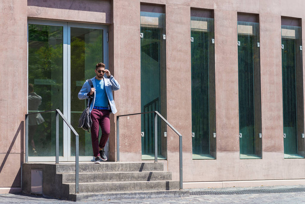 Businessman walking next to office buildings while holding a shoulder bag outdoors - Fotó, kép