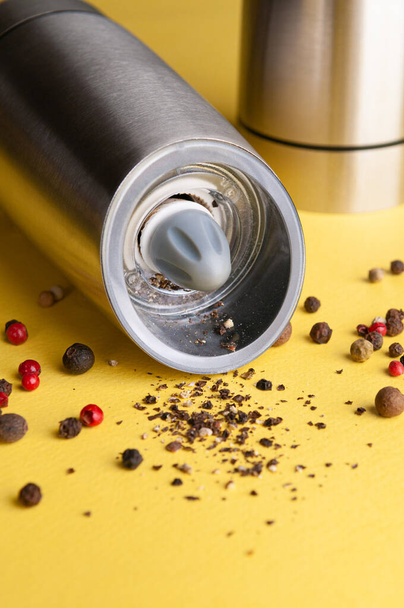 Electric spice mill. Made of metal. Lies on the table. Nearby pepper. Yellow background. Close-up. - Фото, зображення