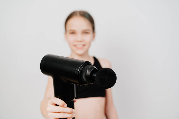 focus on the subject. teen girl holds massage gun. medical-sports device helps to reduce muscle pain after training, helps to relieve fatigue, affects problem areas of body, improves condition of skin - Фото, изображение