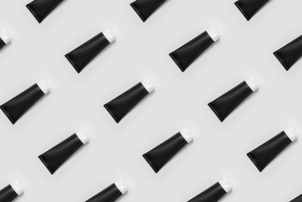 A pattern of black cream tubes on a light gray background. Cosmetic products for the care of the skin of the face, hands, feet and body. - Foto, Imagem