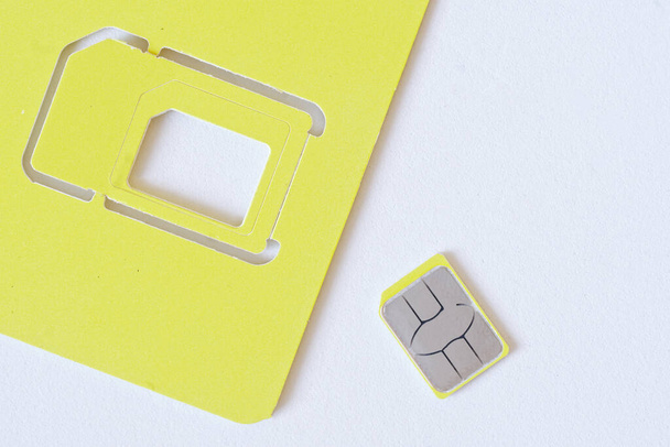 Жовта мініатюрна наноSIM карта для смартфона лежить на білому фоні поруч з пакетом. Цифрові технології та мобільний зв'язок. Макро. Підсумок. - Фото, зображення