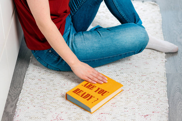 Женщина сидит на полу и держит свою руку на книге с надписью Готовы ли вы руки закрыть вверх. Вид сверху. Концепция готовности к чему-то. - Фото, изображение