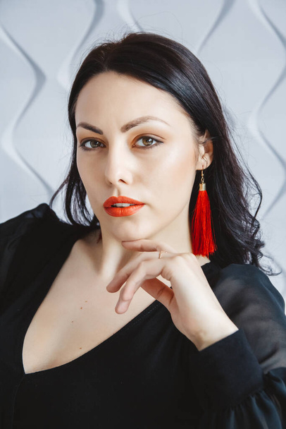 Fashion portrait of a stylish brunette woman wearing a black dress. Woman with long hair wearing red earrings. Posing in studio. Place for text or advertising. - Fotó, kép