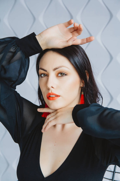 Fashion portrait of a stylish brunette woman wearing a black dress. Woman with long hair wearing red earrings. Posing in studio. Place for text or advertising. - 写真・画像