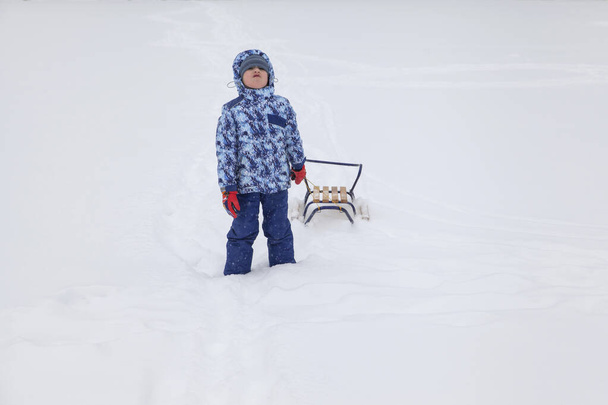 маленький хлопчик в зимовому одязі з санчатами у важкому снігу
 - Фото, зображення