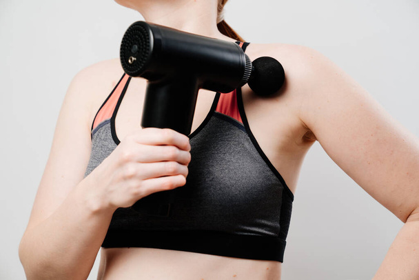 woman holds massage gun. medical-sports device helps to reduce muscle pain after training, helps to relieve fatigue, affects problem areas of body, improves condition of skin. - Photo, Image