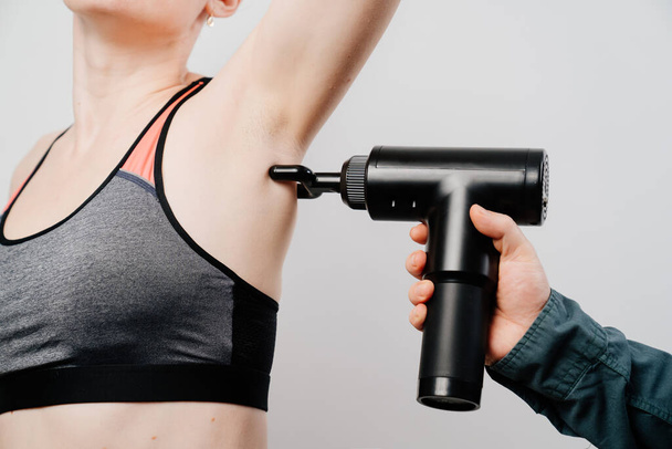 woman uses massage gun. medical-sports device helps to reduce muscle pain after training, helps to relieve fatigue, affects problem areas of body, improves condition of skin. - Photo, Image