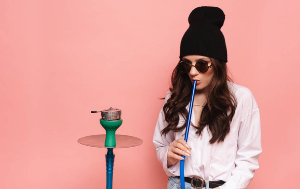 Una giovane donna in un'immagine hipster fuma un narghilè, sheesha e gode di fumare. - Foto, immagini