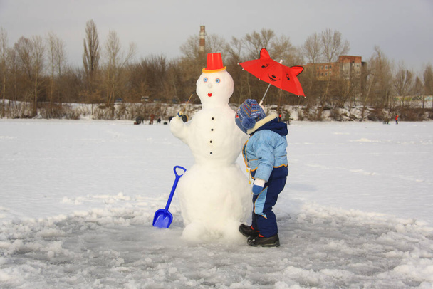 niño pequeño en ropa de invierno haciendo un muñeco de nieve - Foto, Imagen