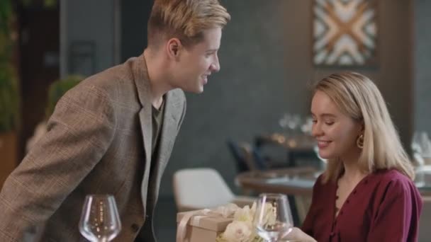 Střední detailní záběr romantického páru na první den s večeří v luxusní restauraci, flirtování a smích, muž dárky květiny a dárek box - Záběry, video