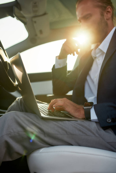 Laptop in hands of young working businessman in car - Фото, зображення