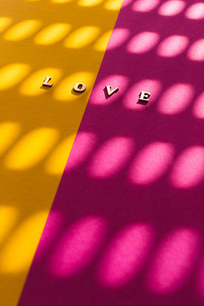 Word LOVE, fait de lettres en bois, divisé entre deux fonds vibrants - couleur jaune et rose  - Photo, image