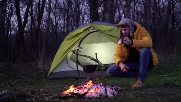 Un uomo vicino a un falò e una tenda nella foresta - Filmati, video