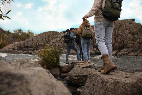 Group of friends with backpacks crossing mountain river, focus on hiking boots - Photo, Image