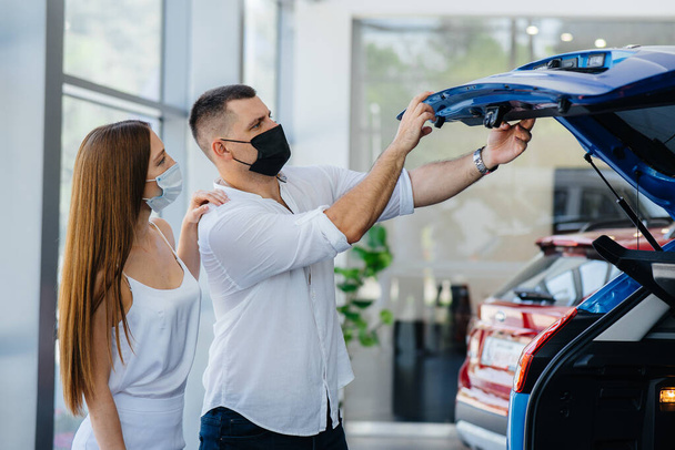 Young couple in masks selects a new vehicle and consult with a representative of the dealership in the period of the pandemic. Car sales, and life during the pandemic - Фото, изображение