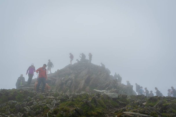 イギリス、スノードン。07-08-2020 。2020年8月に英国がパンデミック対策を緩和すると、「在留期間の休日」が急増しました。ハイキング中にキューに待っている霧と霧の日自分撮りを取るためにスノードン山のピークにアクセスするために順番に. - 写真・画像