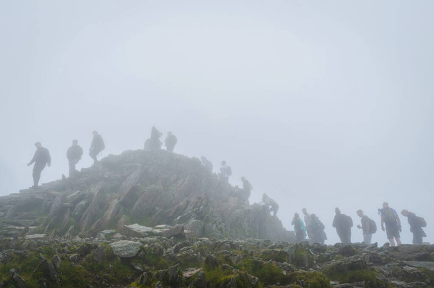 Snowdon, UK. 07-08-2020. When UK relaxed pandemic lockdown rules in August 2020 it resulted in surge of ''stay-cation holidays''. Hikers awaits in a queue during foggy and misty day for their turn to access peak of mount Snowdon to take a selfie. - Photo, Image
