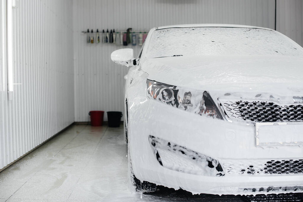 Modern washing with foam and high-pressure water of a white car. Car wash - Zdjęcie, obraz