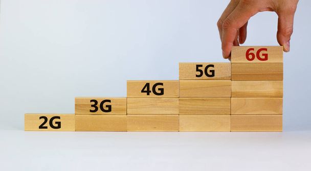 6G network evolution symbol. Hand holding a wooden block with 6g symbol. 2G, 3G, 4G, 5G words. Copy space. Beautiful white background. Technology, business, communication and 6G concept. - Фото, изображение