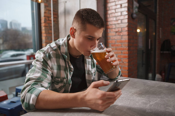 Man sipping craft beer whle browsing online on his smart phone - Φωτογραφία, εικόνα