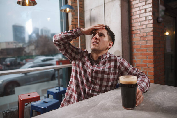 Nuori mies näyttää murtuneelta, katsomassa peliä ruudulla olutpubissa - Valokuva, kuva
