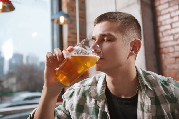 Primer plano de un hombre bebiendo deliciosa cerveza artesanal con los ojos cerrados de placer - Foto, Imagen