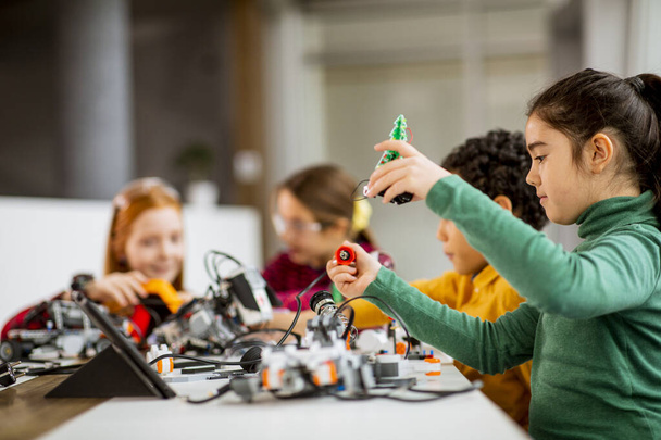 Grupa szczęśliwych dzieci programuje zabawki elektryczne i roboty w klasie robotyki - Zdjęcie, obraz