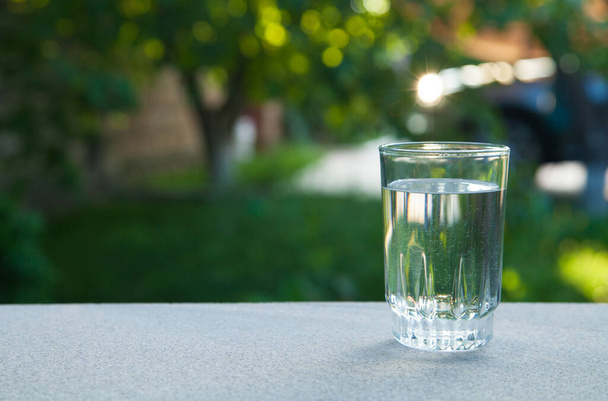 Drinking water glass against the background of green nature. - Foto, afbeelding