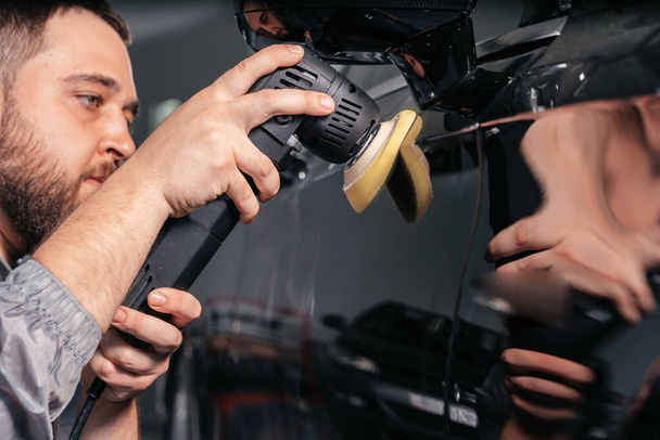 Worker polishing car with special grinder and wax from scratches at the car service station. Professional car detailing and maintenance concept - Φωτογραφία, εικόνα