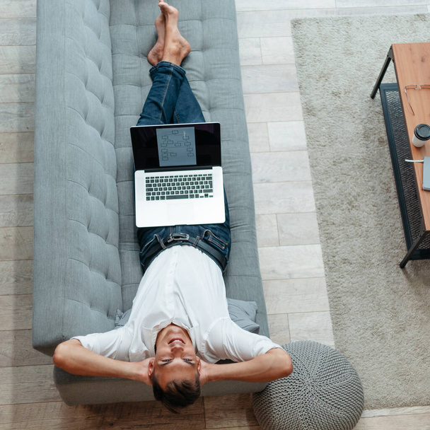 happy man with a laptop lying on the couch . - Foto, Bild
