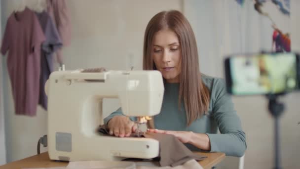 Medium shot of caucasian woman filming video tutorial lesson on smartphone of how to use sewing machine at home talking on camera - Footage, Video