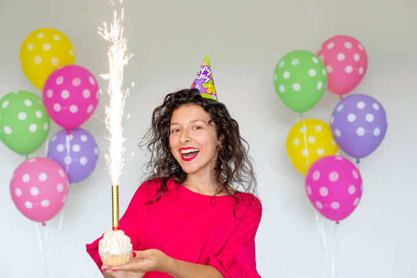 Happy Birthday. Sexy brunette girl posing with balloons, fireworks, colorful balloons and holiday cake on a white background. - Φωτογραφία, εικόνα