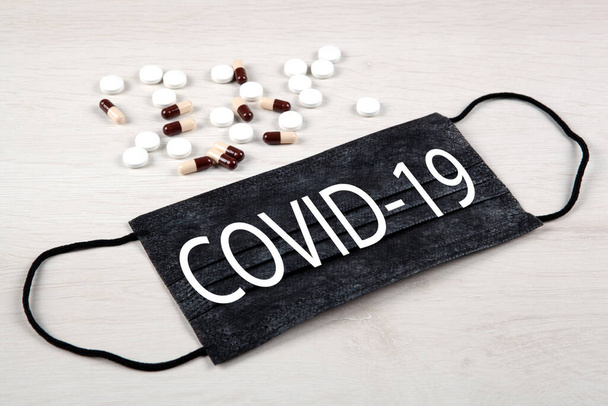 lääketieteellinen naamio, jossa merkintä covid-19 ja lääkkeet pöydällä - Valokuva, kuva
