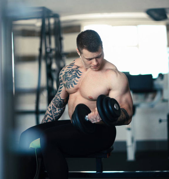 muscular bodybuilder with dumbbells sitting on a bench in the gym - Φωτογραφία, εικόνα