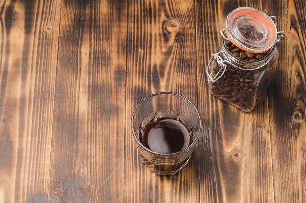 Glass of cofee with cofee beans. Top view and copy space. Cup of black coffee in a glass and grains in a glass jar on a wooden table.  - Foto, Imagem