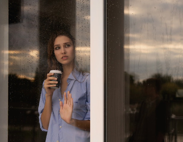 beautiful young woman with coffee cup looking through the window - Foto, imagen