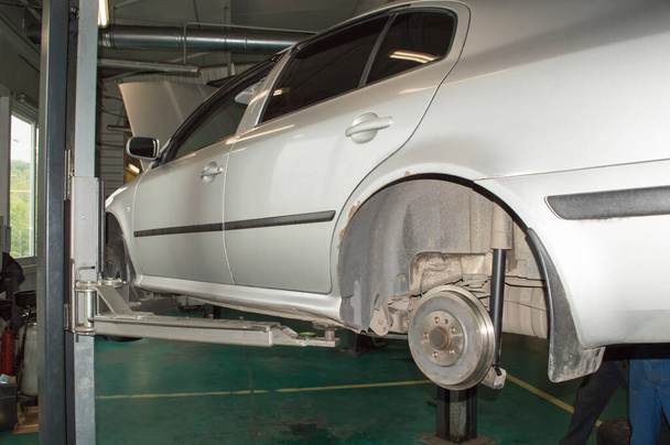 Vervanging van de achterremtrommels op een grijze auto die in een garage aan een grijze lift hangt - Foto, afbeelding
