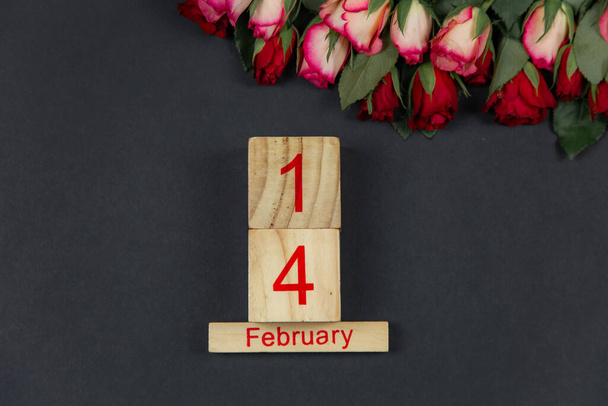 Rote Rosen für den Feiertag auf dunklem Hintergrund mit Holzkalender. Platz für Text zum Valentinstag, 14. Februar - Foto, Bild