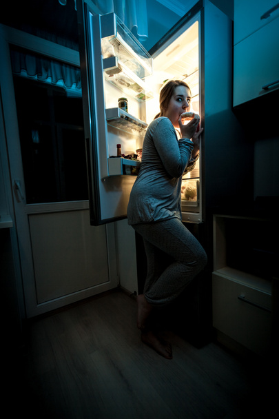 éhes nő eszik éjjel közelében hűtőszekrény - Fotó, kép