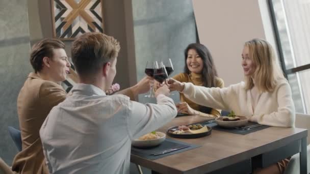 Μέτριο πλάνο των χαρούμενων ομάδα ανθρώπων που έχουν διπλό ραντεβού clinking ποτήρια κόκκινο κρασί κάθεται στο τραπέζι στο σύγχρονο εστιατόριο - Πλάνα, βίντεο